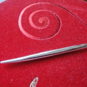 Könnte beinhalten: Ein silberfarbener Häkelhaken mit einer spitzen Spitze und einer kleinen Schlaufe am Ende.