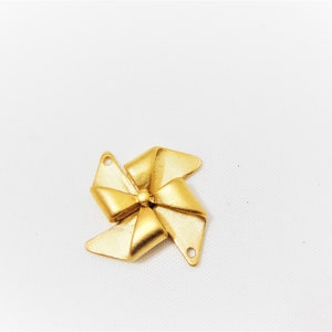 May include: A gold-colored metal bow charm with a five-pointed star design. The charm has two holes for attaching to a necklace or bracelet.