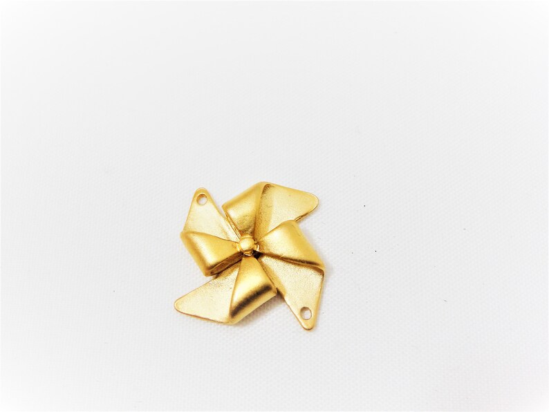 May include: A gold-colored metal bow charm with a five-pointed star design. The charm has two holes for attaching to a necklace or bracelet.