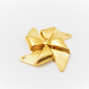 May include: Gold-toned metal charm shaped like a bow with a pinwheel design. The charm has two holes for attaching to jewelry or other crafts.