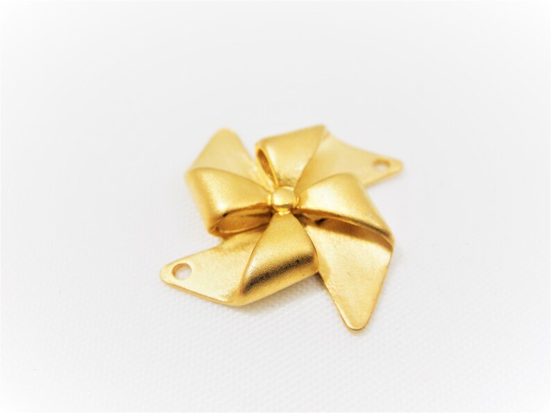 May include: Gold-toned metal charm shaped like a bow with a pinwheel design. The charm has two holes for attaching to jewelry or other crafts.