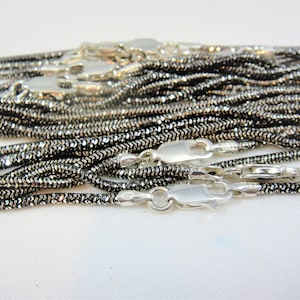 May include: A close-up of a pile of silver snake chains with a sparkly finish. The chains are all the same length and have a lobster clasp.