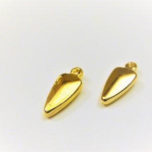 Puede incluir: Dos abalorios de metal de color dorado en forma de lágrima con un bucle en la parte superior.