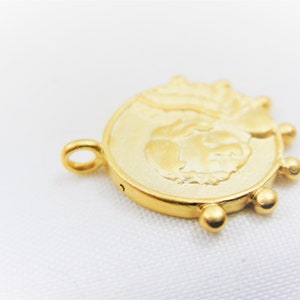 May include: Gold-toned metal charm featuring a raised design of a face with a crown. The charm has a loop for attaching to a necklace or bracelet and a series of small beads around the edge.