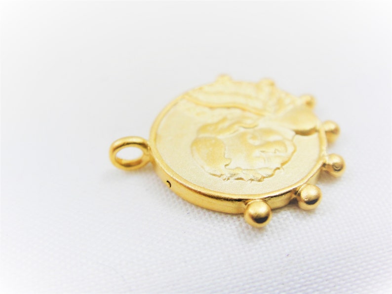 May include: Gold-toned metal charm featuring a raised design of a face with a crown. The charm has a loop for attaching to a necklace or bracelet and a series of small beads around the edge.