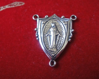 May include: Silver-toned metal rosary charm featuring a depiction of the Virgin Mary in a shield-shaped frame.