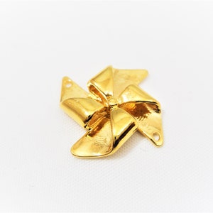 May include: Gold-toned metal charm shaped like a pinwheel with a bow design. The charm has two holes for attaching to jewelry.