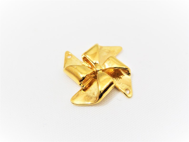 May include: Gold-toned metal charm shaped like a pinwheel with a bow design. The charm has two holes for attaching to jewelry.