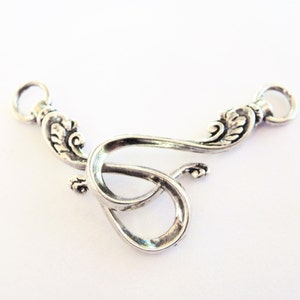 May include: Silver-toned metal connector with two loops and a decorative design. The connector is shaped like a stylized letter S.
