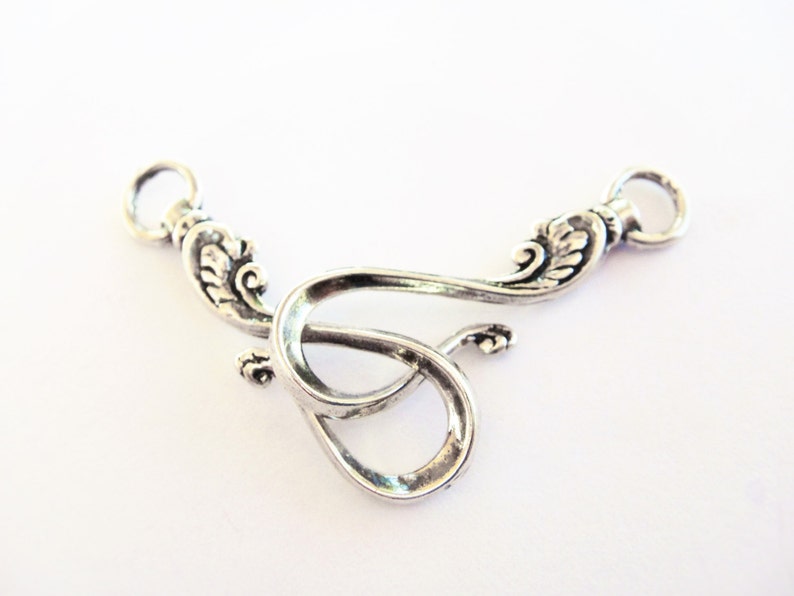 May include: Silver-toned metal connector with two loops and a decorative design. The connector is shaped like a stylized letter S.