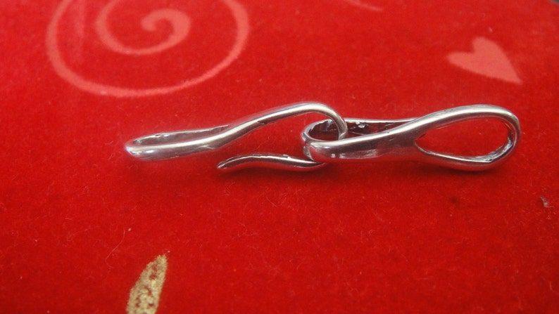 May include: Silver clasp with a curved design, suitable for attaching to a necklace or bracelet.
