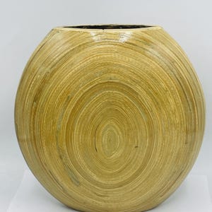 May include: A round, light brown, woven bamboo vase. The vase has a smooth, glossy finish and a circular pattern.