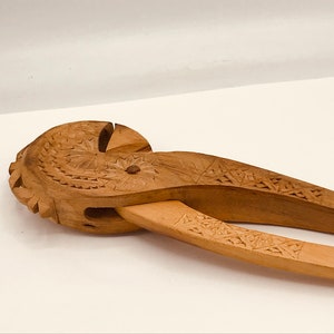 May include: A wooden nutcracker with intricate carvings. The nutcracker is made of light brown wood and has a detailed design on the handles.