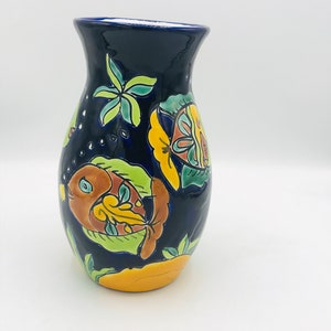 May include: A blue ceramic vase with a floral and fish design. The vase is decorated with yellow, green, orange, and brown paint.