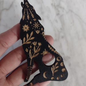 May include: Black wooden cutout of a howling wolf with gold floral and moon designs.