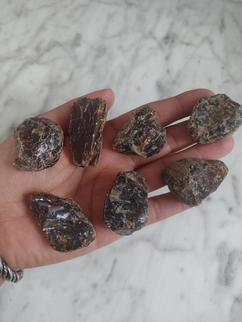 May include: A collection of seven dark brown amber stones of various shapes and sizes. The stones are smooth and have a glossy finish.