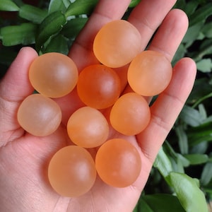 May include: A collection of ten smooth, round, orange-colored glass beads. The beads are translucent and have a slight shimmer.