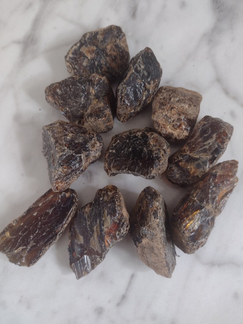 May include: A collection of ten dark amber stones with a variety of shapes and sizes. The stones have a rough, natural texture and a deep, rich color.