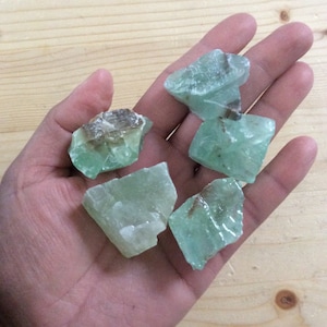 May include: Five rough-cut green and white calcite crystals with brown inclusions. The crystals are translucent and have a variety of shapes and sizes.