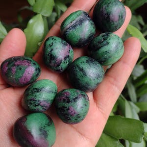 May include: A collection of eight green, black, and pink tumbled stones. The stones are smooth and polished, and they have a variety of patterns and textures.