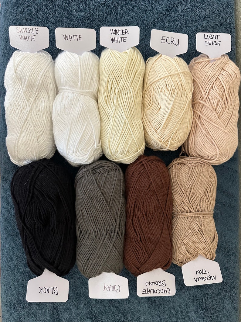 Puede incluir: Diez ovillos de lana en varios colores, incluyendo blanco, beige, marr&oacute;n, gris y negro. Los ovillos de lana est&aacute;n etiquetados con sus nombres de color.