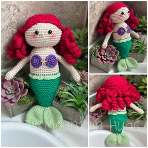 Puede incluir: Mu&ntilde;eca de sirena de crochet con pelo rojo, un top de concha de mar morado y dorado y una cola verde. La mu&ntilde;eca est&aacute; sentada sobre una superficie blanca con plantas verdes en macetas.