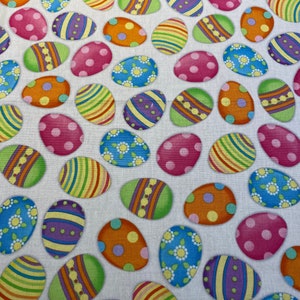 May include: A white fabric with a repeating pattern of colorful Easter eggs. The eggs are decorated with stripes, polka dots, and floral designs.