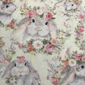 May include: A light green fabric with a repeating pattern of gray bunnies wearing floral crowns. The bunnies are surrounded by pink, white, and purple flowers.