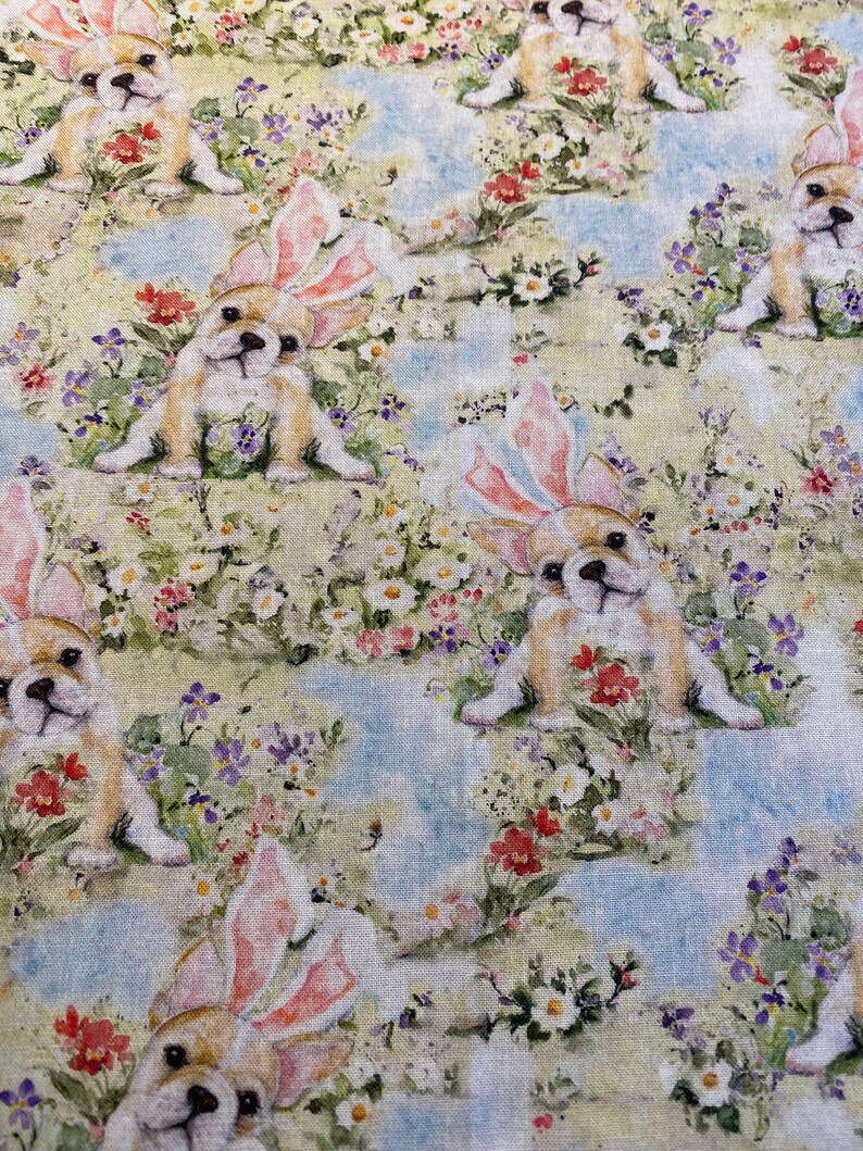 May include: A repeating pattern of white, brown, and pink bunny-eared puppies on a light blue and green floral background.