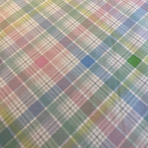 May include: A white fabric with a multicolored plaid pattern. The plaid pattern features shades of pink, blue, green, and yellow.