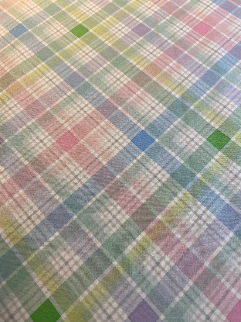 May include: A white fabric with a multicolored plaid pattern. The plaid pattern features shades of pink, blue, green, and yellow.
