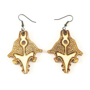 May include: A pair of wooden earrings with a detailed, intricate design. The earrings are light brown in color and have a unique, organic shape.