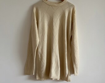 May include: A cream-colored sweater with a diamond pattern knit. The sweater has long sleeves and a round neckline.