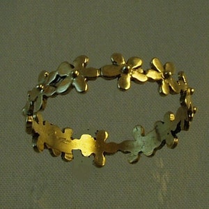 Peut inclure: Une bague en or avec un motif floral. La bague est faite d'une fine bande de m&eacute;tal avec de petits d&eacute;tails en forme de fleurs.