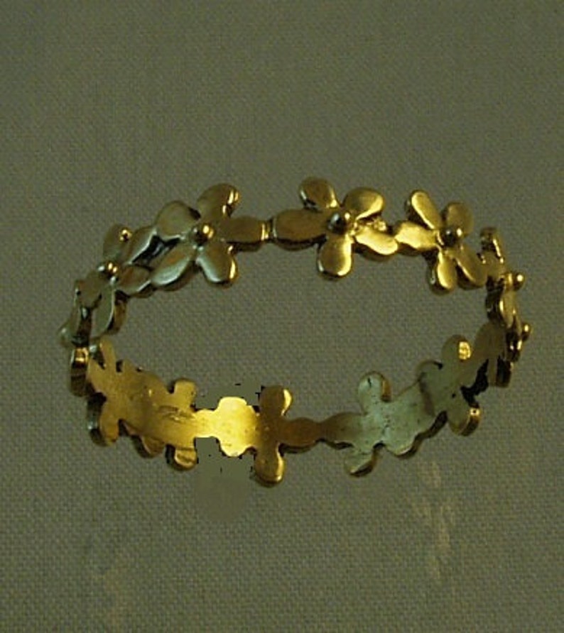 Peut inclure: Une bague en or avec un motif floral. La bague est faite d'une fine bande de m&eacute;tal avec de petits d&eacute;tails en forme de fleurs.
