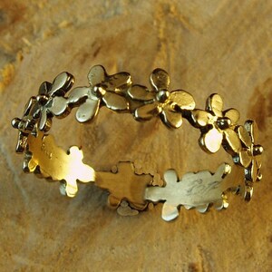 Peut inclure: Une bague en or avec un motif d&eacute;licat de petites fleurs. La bague est en m&eacute;tal lisse et brillant et a un aspect simple et &eacute;l&eacute;gant.