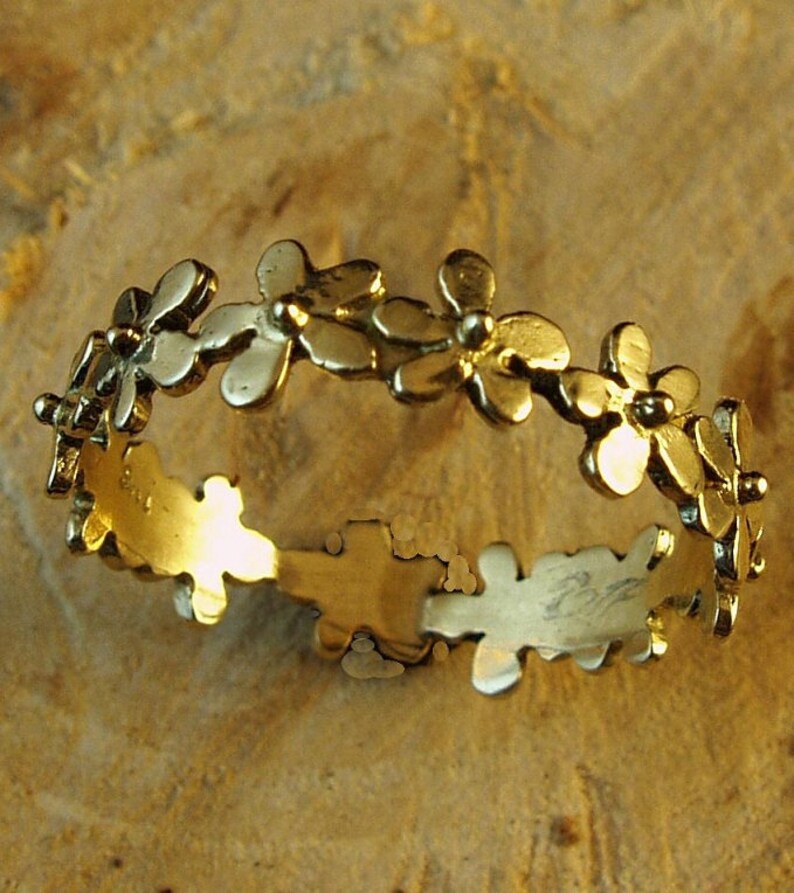 Peut inclure: Une bague en or avec un motif d&eacute;licat de petites fleurs. La bague est en m&eacute;tal lisse et brillant et a un aspect simple et &eacute;l&eacute;gant.
