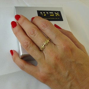 Peut inclure: Une bague en or avec un d&eacute;licat motif floral. La bague est port&eacute;e sur le doigt d'une main avec du vernis &agrave; ongles rouge.