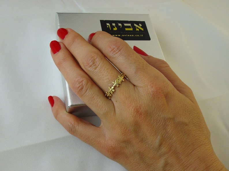 Peut inclure: Une bague en or avec un d&eacute;licat motif floral. La bague est port&eacute;e sur le doigt d'une main avec du vernis &agrave; ongles rouge.