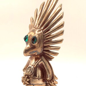 May include: A gold-coloured figurine of a creature with a spiky mohawk, green eyes, and a flower in its hand.