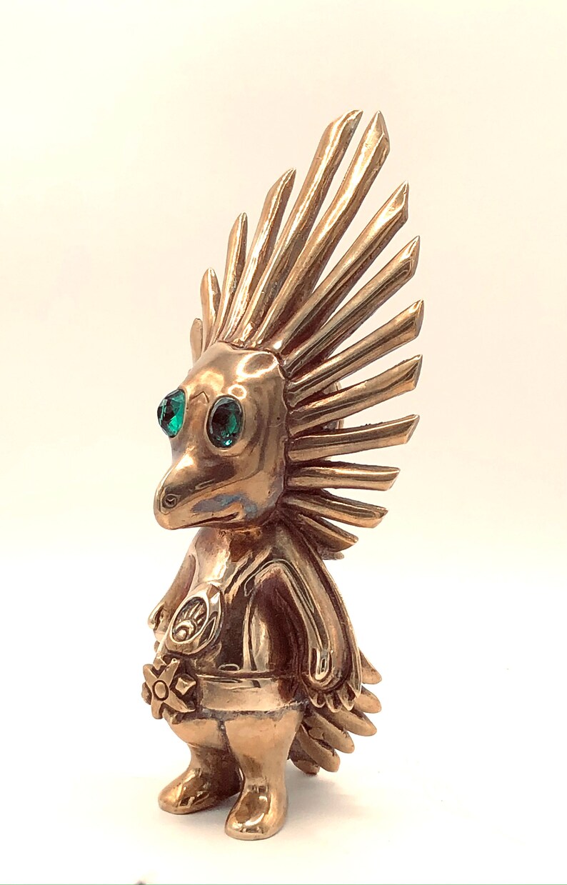 May include: A gold-coloured figurine of a creature with a spiky mohawk, green eyes, and a flower in its hand.