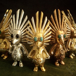 May include: A group of five silver, gold, and bronze figurines with turquoise and black eyes. Each figurine has a spiky crown and a bird-like beak. The figurines are arranged in a circle.