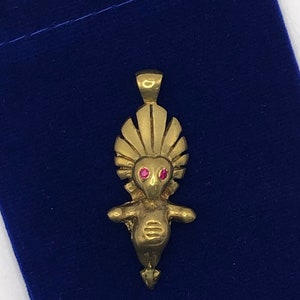 May include: A gold pendant featuring a stylised human figure with a crown of feathers and red gemstone eyes.