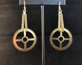 Peut inclure: Boucles d'oreilles dorées avec un motif d'engrenage suspendu et une chaîne attachée au sommet.