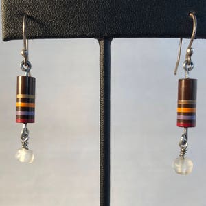 May include: A pair of dangle earrings with dark brown cylindrical beads accented with horizontal stripes in gold, orange, purple, and red. Each earring has a small, clear, round bead at the bottom and silver-tone ear wires.