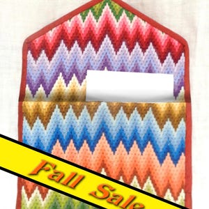 May include: A colorful, handmade wall pocket with a chevron pattern in shades of red, purple, blue, orange, and green. The pocket has a red border and a small loop at the top. The words "Fall Sale" are displayed on a yellow banner.