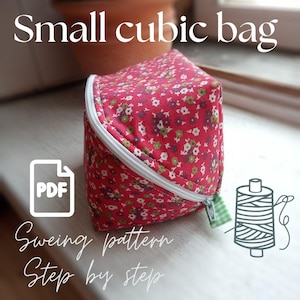 May include: A small cubic bag featuring a red fabric with a white, green, and purple floral pattern. The bag has a white zipper closure and a small green and white checkered fabric tab. Text on the image reads Small cubic bag, PDF, and Sewing pattern Step by step.