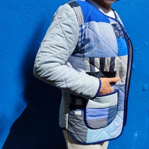 Pode incluir: Uma jaqueta acolchoada azul feita de tecido patchwork. A jaqueta tem um padrão xadrez azul e branco e uma guarnição azul marinho.