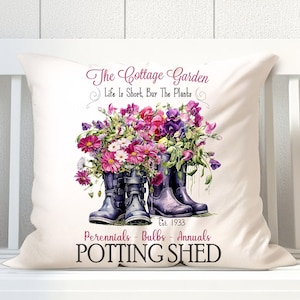 May include: A white cushion with a floral design featuring purple and pink flowers in blue wellies. The text on the cushion reads "The Cottage Garden, Life Is Short, Buy The Plants, Est. 1933, Perennials - Bulbs - Annuals, POTTING SHED".