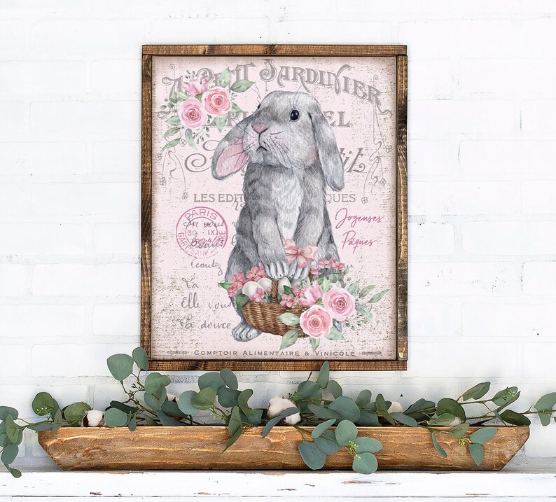 May include: A vintage-style print featuring a gray bunny rabbit holding a basket of pink flowers. The print has a pink background with French text that reads "Le Petit Jardinier" and "Comptoir Alimentaire & Vinicole".
